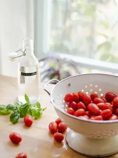 Pomodori rossi in colino bianco rotondo con menta verde e bottiglia di vetro