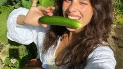 Donna sorridente con cetriolo fresco in giardino soleggiato